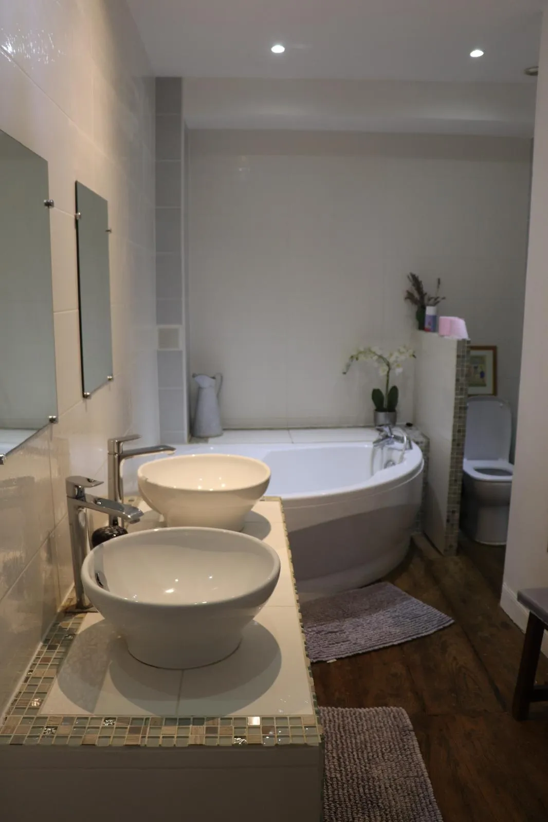 Salle de bain claire avec baignoire d’angle, double vasque et WC séparé