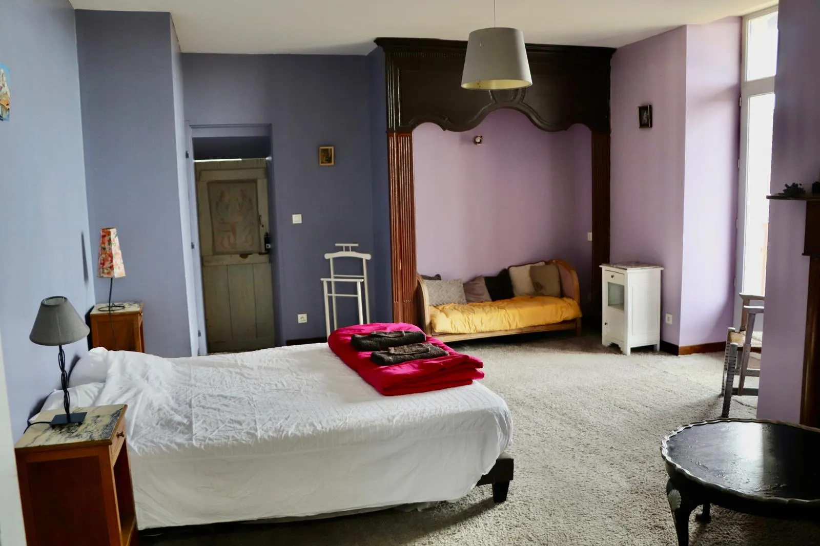 Grande chambre aux murs mauves, lit double et alcôve en bois abritant une banquette