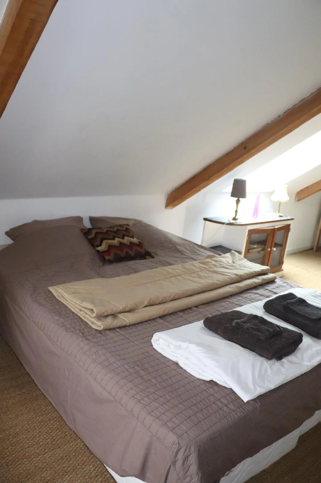 Lit double sous les combles, poutres blanchies et petit vaisselier vitré