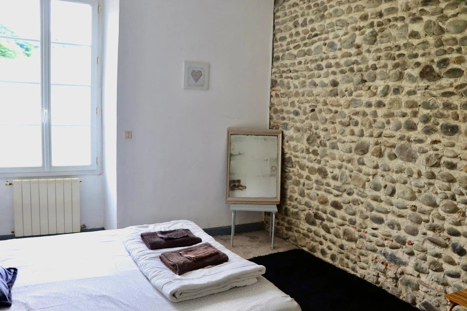 Chambre au mur de galets apparents, lit double face à une fenêtre donnant sur le jardin