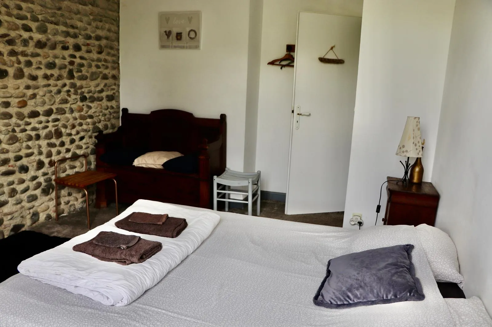 Chambre avec mur de galets, lit double et banc en bois ancien