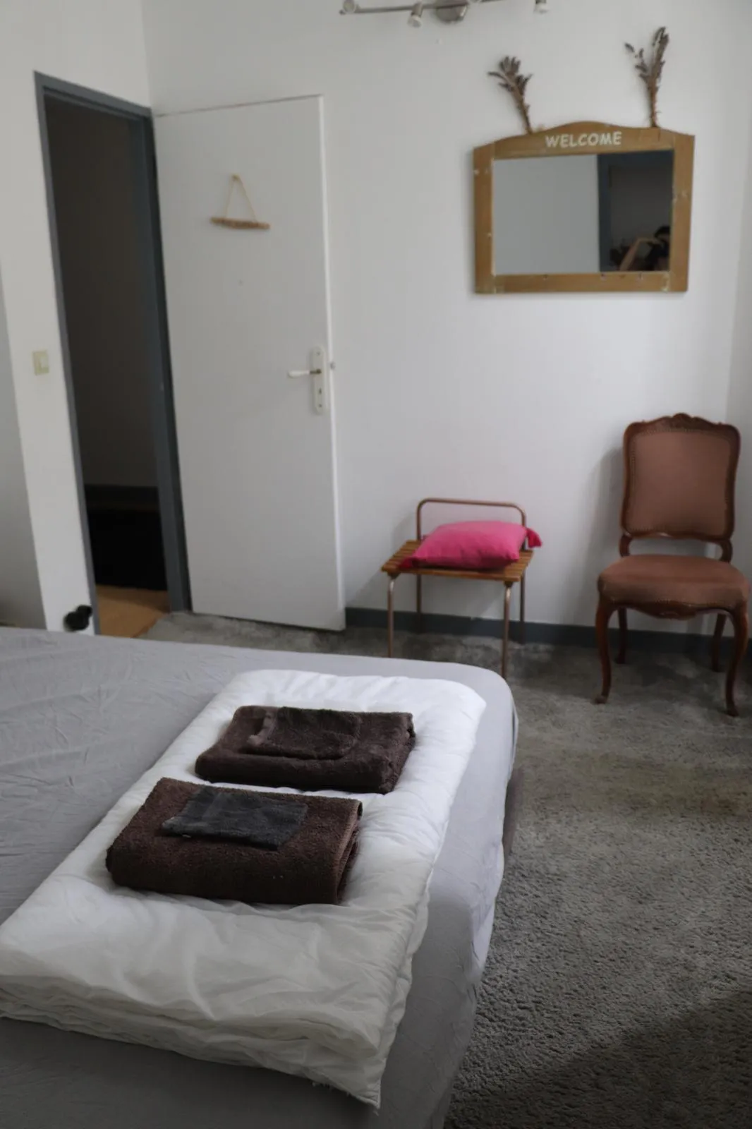 Chambre avec miroir ancien, chaise et petite table, porte ouvrant sur le palier
