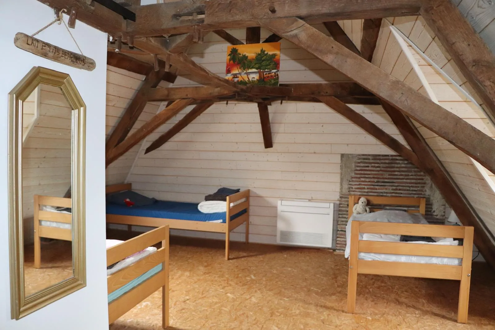 Dortoir aménagé sous la charpente d’origine, lits simples alignés entre les fermes en bois