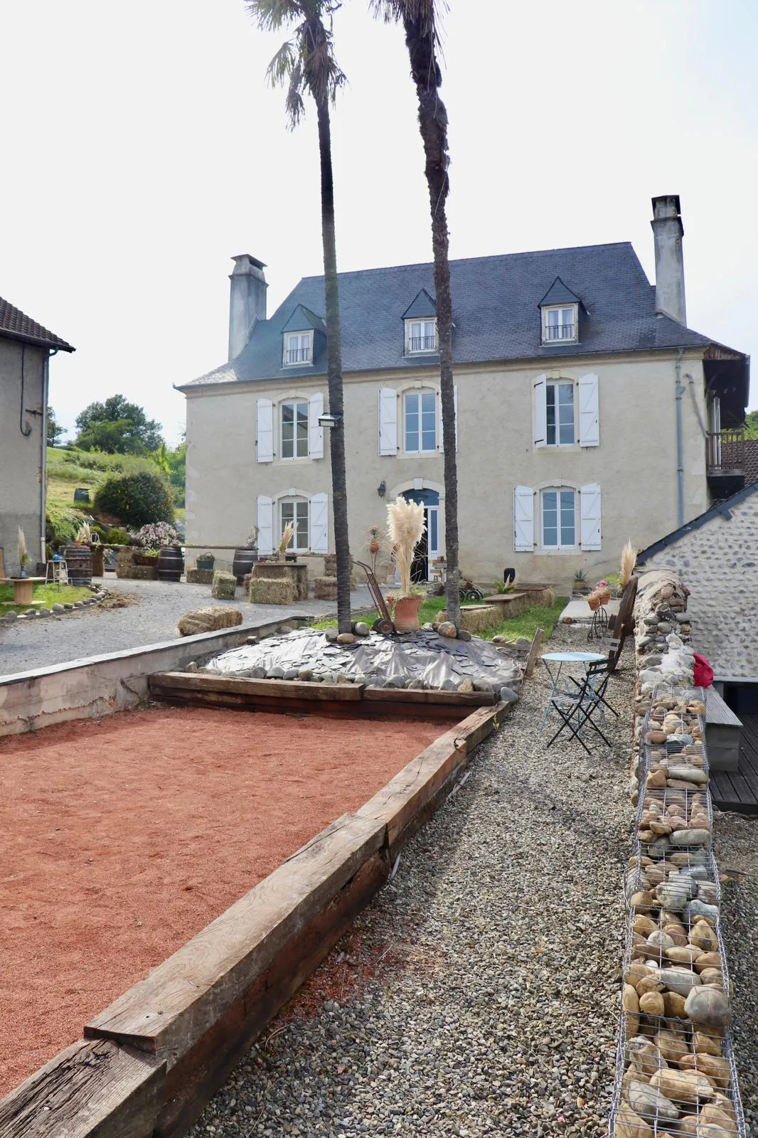 Terrain de pétanque en terre battue devant la maison béarnaise à volets bleus