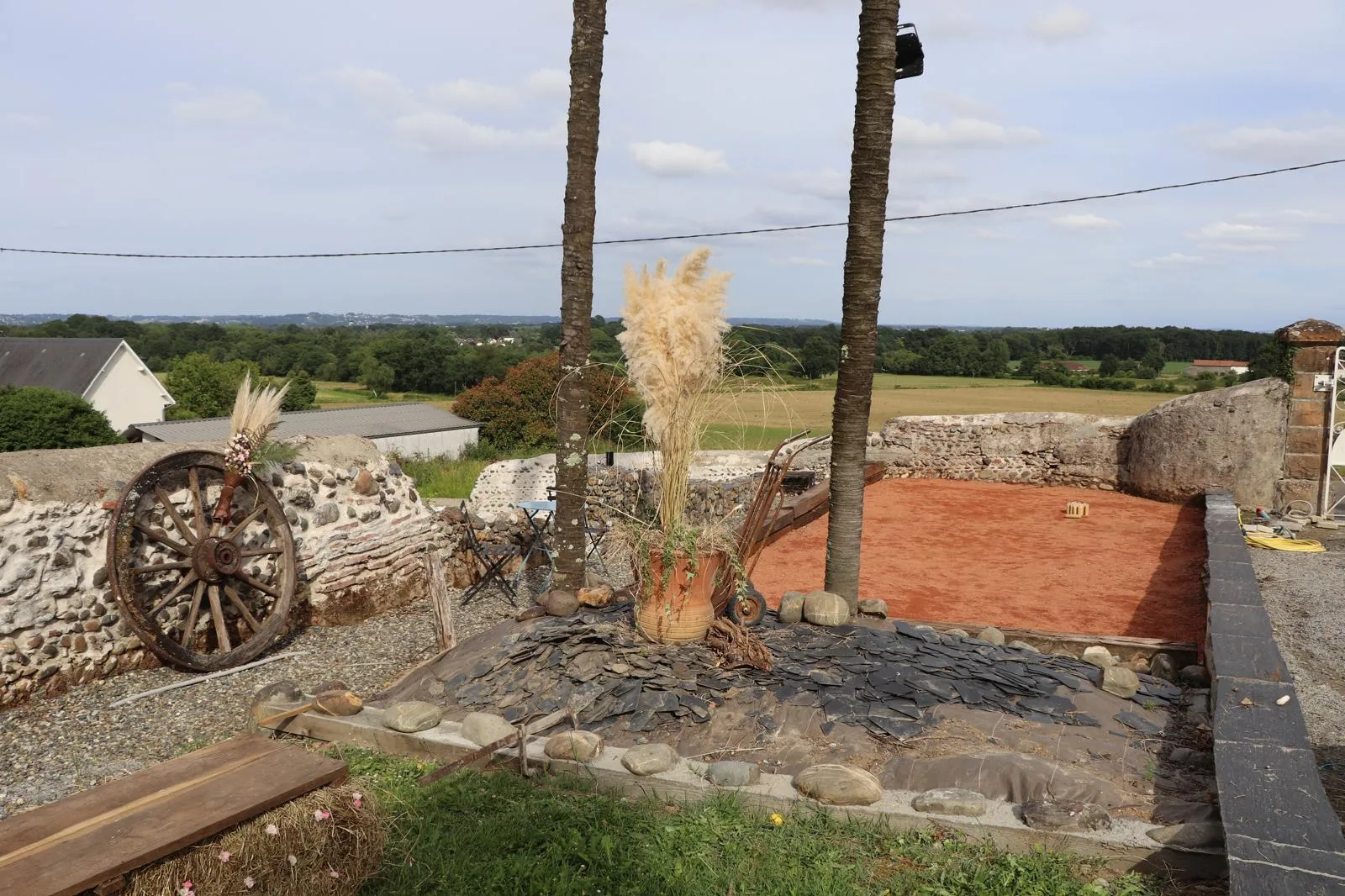Ancienne roue de charrette adossée au mur de galets, à côté du terrain de pétanque