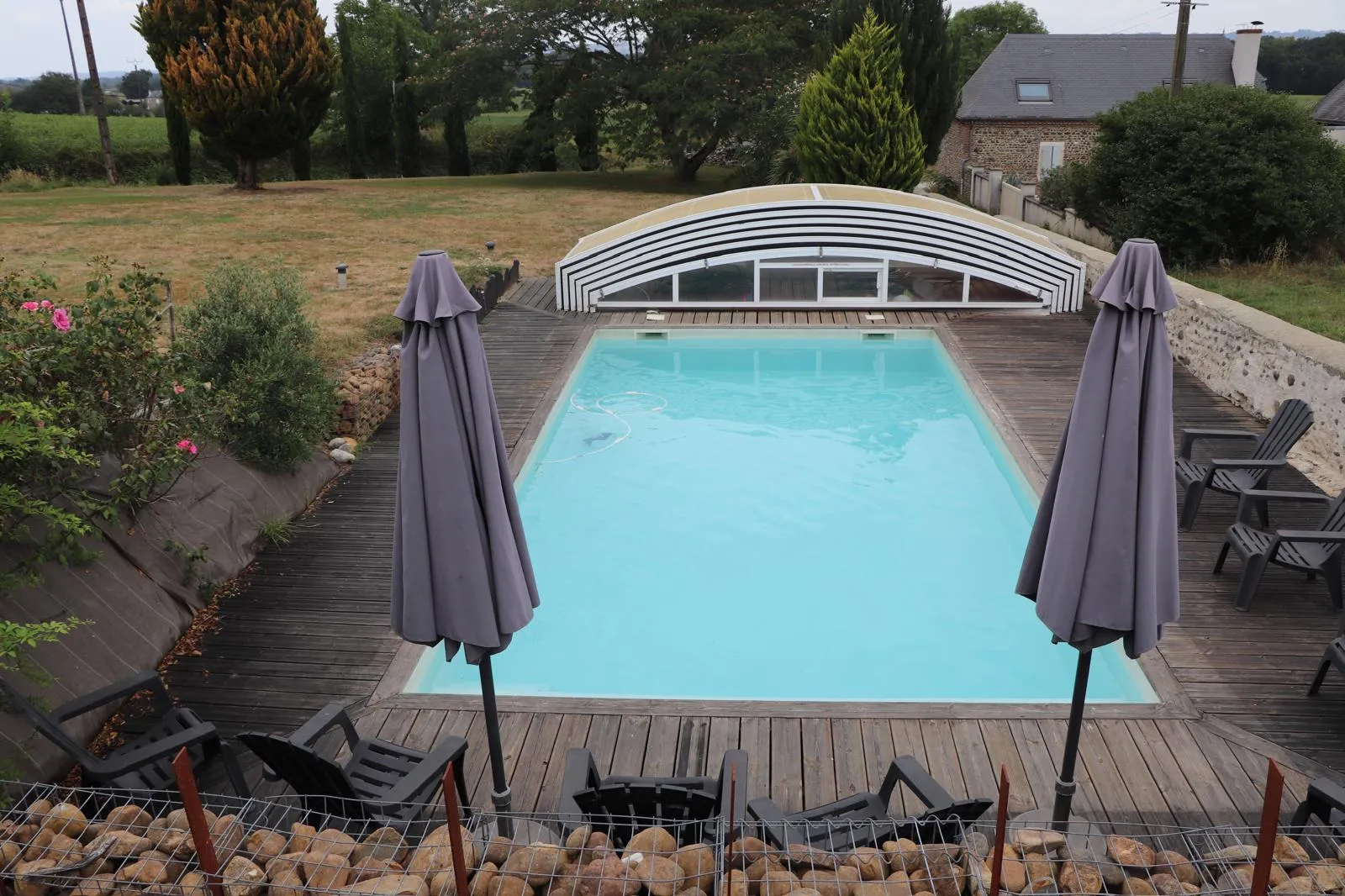 Piscine rectangulaire avec son abri télescopique replié à une extrémité, parasols fermés sur la terrasse