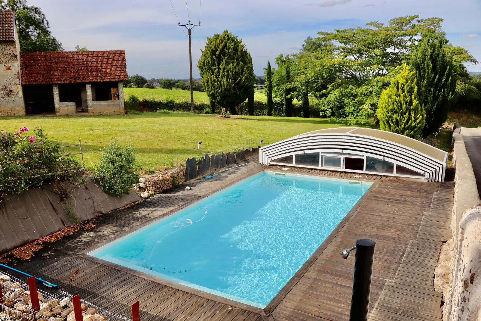 La piscine avec la vieille grange en pierre et les prairies derrière
