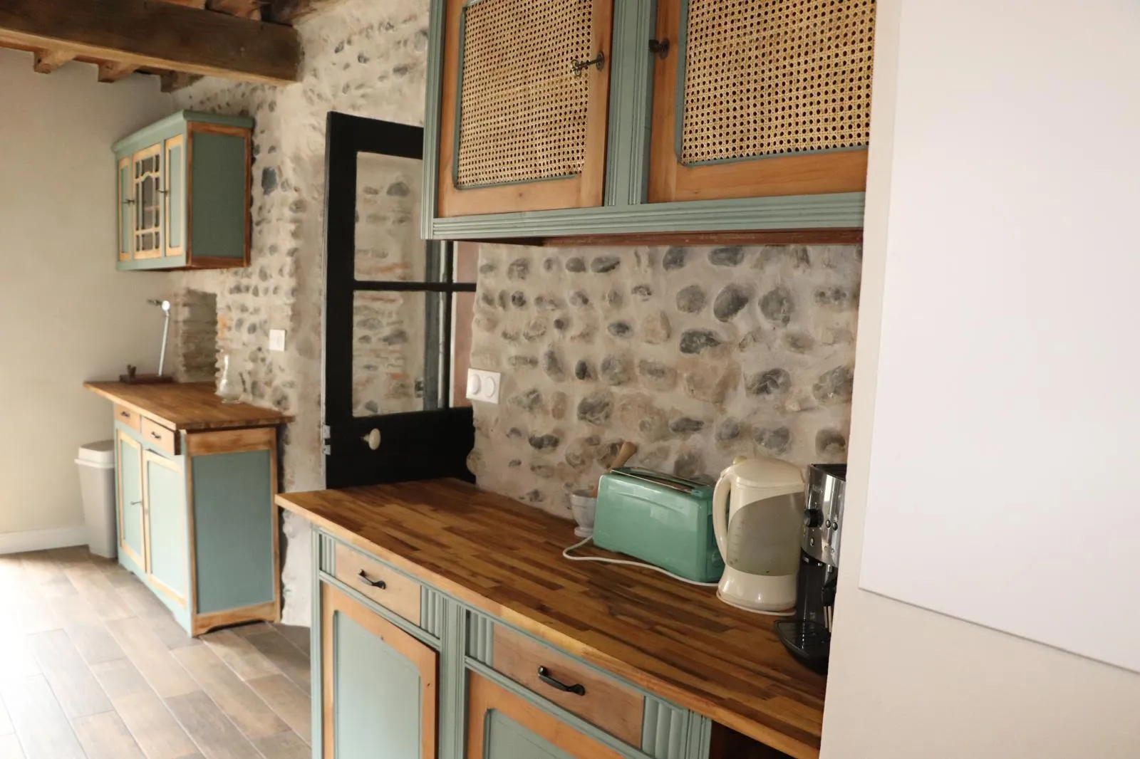 Buffet ancien repeint, bouilloire et grille-pain sur le plan de travail en bois, mur de galets