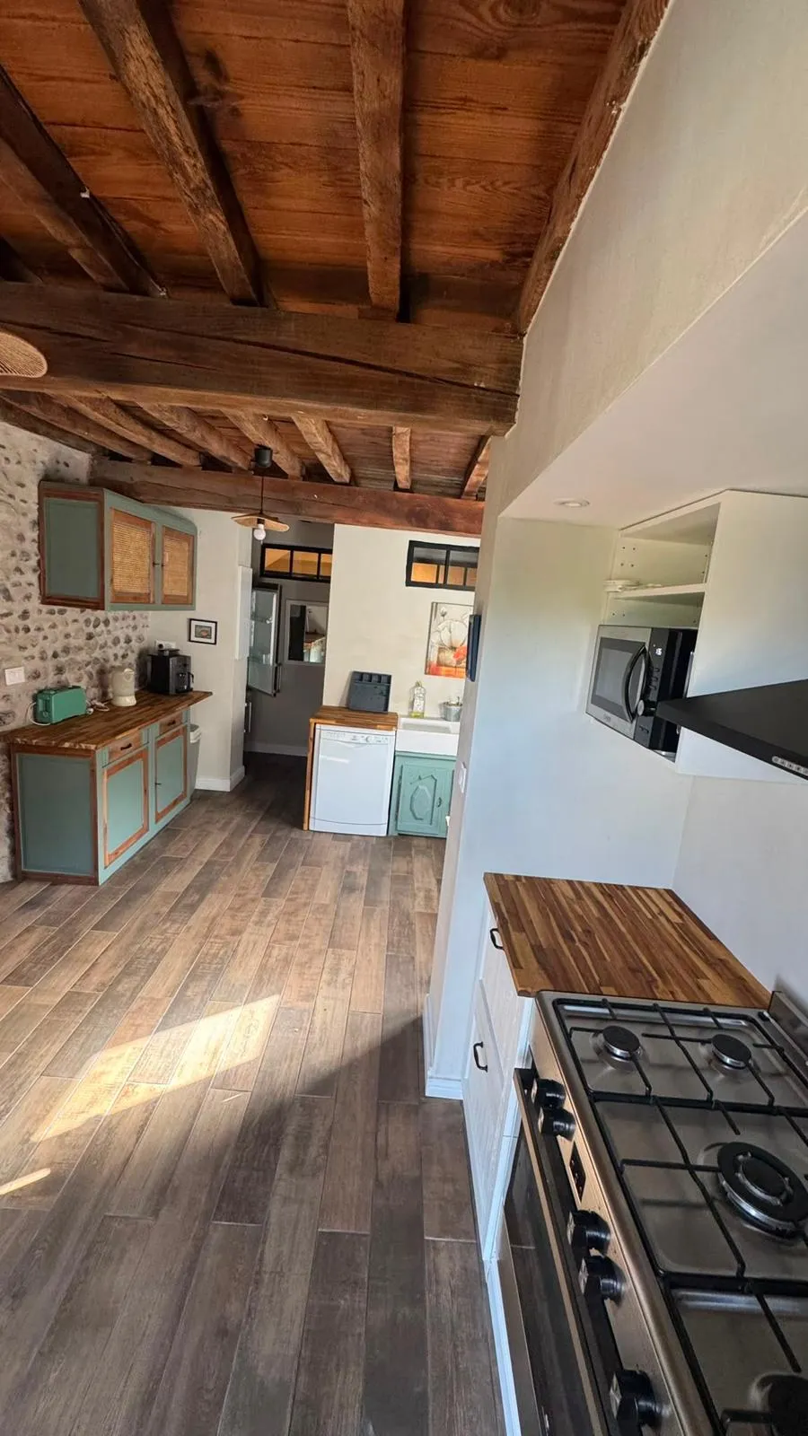 La cuisine en enfilade, sol en bois et plafond à poutres sombres