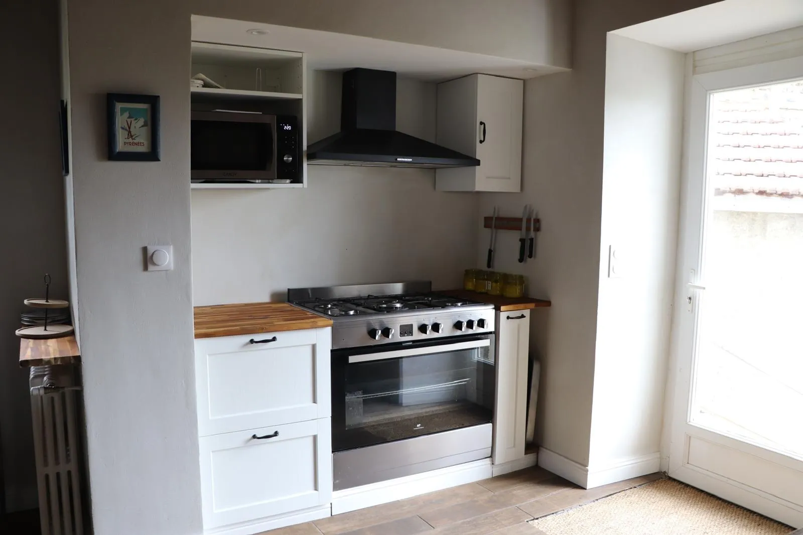 Piano de cuisson cinq feux en inox sous sa hotte, encadré de meubles blancs