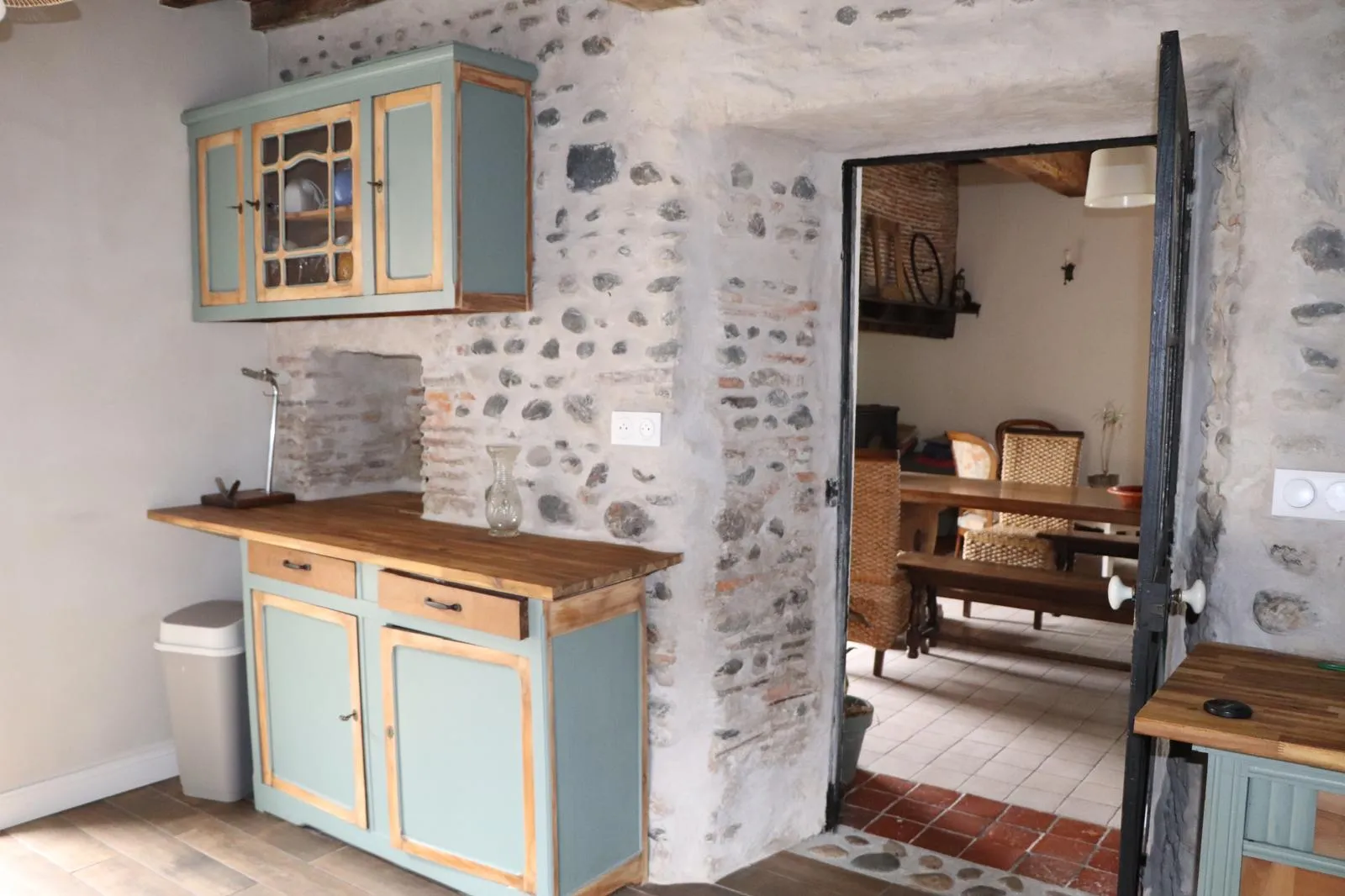 Enfilade de la cuisine vers le salon, à travers une porte en bois dans un mur de galets