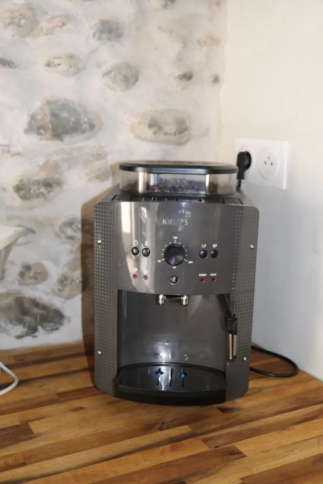 Machine à café à grains posée sur un plan de travail en bois, devant un mur de galets